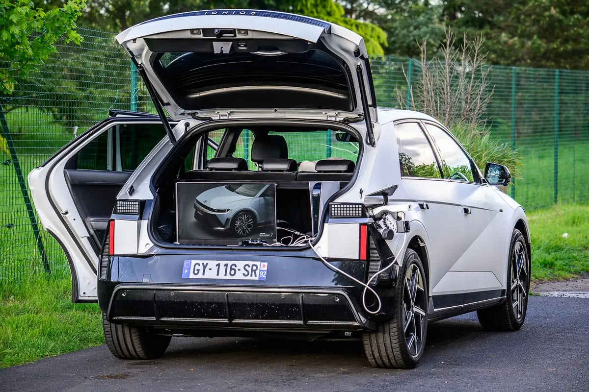 Conduire une Ioniq 5 dans Gran Turismo 7, l'&eacute;cran dans le coffre de la Ioniq 5, en &eacute;tant branch&eacute; &agrave; une Ioniq 5. Une "Inception" sign&eacute; le V2L
